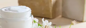 Glass jar of moisturizing cream and almond blossoms on wooden background