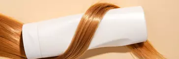 Blond hair with shampoo bottle close-up on light background, copy space