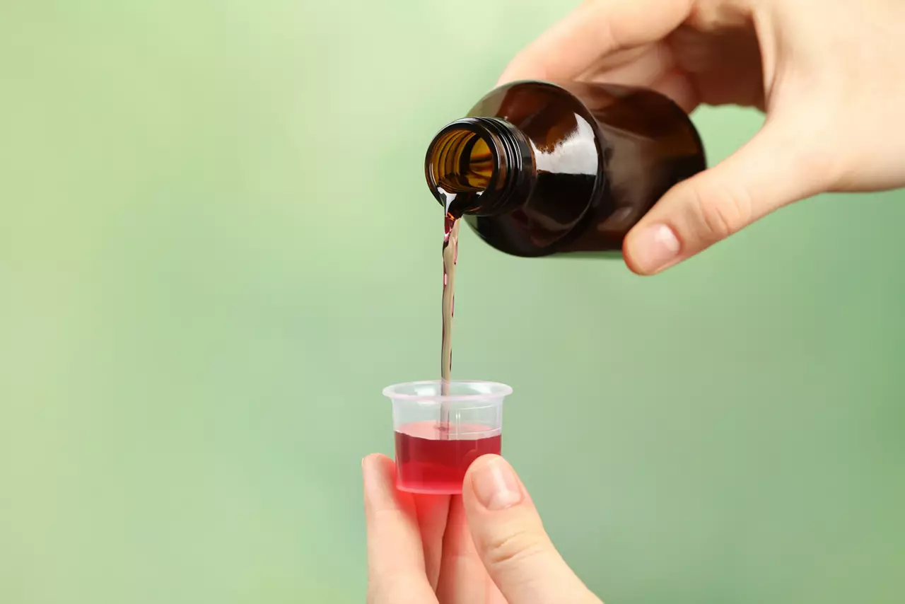 Woman pouring cough syrup into measuring cup on light green background, closeup